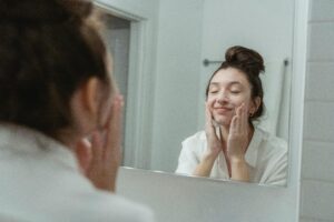 Woman applying soap to her face, reflected in the bathroom mirror, enjoying a skincare routine.