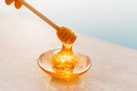 10 Home Remedies for Glowing Skin Golden honey flowing from a wooden dipper onto a glass plate, captured in warm daylight.